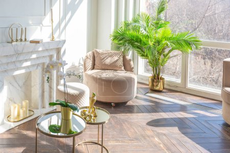 interior muy ligero y luminoso de lujoso y acogedor salón con elegantes muebles de color beige suave con elementos metálicos de oro, gran ventana al suelo y parquet de madera