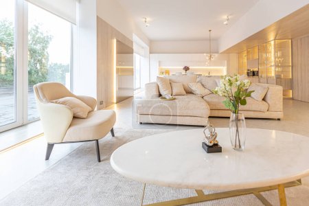 moderno diseño interior moderno de un gran estudio en colores blanco y beige con grandes ventanales de suelo a techo. zona de cocina blanca con una isla y una zona de recreo