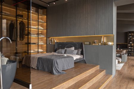 chambre et salle de bain indépendante derrière une cloison en verre dans un intérieur chic et coûteux d'une maison de luxe avec un design moderne sombre avec garniture en bois et lumière led