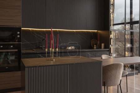 Téléchargez les photos : Coin cuisine dans un intérieur chic et cher d'une maison de luxe avec un design moderne noir foncé et marron avec garniture en bois et lumière led - en image libre de droit
