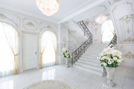 Photo for Luxury royal posh interior in baroque style. very bright, light and white hall with expensive oldstyle furniture. chic wide marble staircase leading to the second floor - Royalty Free Image