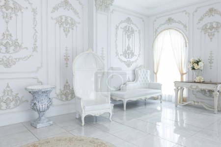 Foto de Interior elegante real de lujo en estilo barroco. vestíbulo muy luminoso, ligero y blanco con muebles de estilo antiguo caros. grandes ventanas y adornos de estuco en las paredes - Imagen libre de derechos