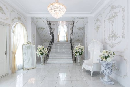 Téléchargez les photos : Luxueux intérieur royal chic dans un style baroque. hall très lumineux, lumineux et blanc avec meubles de style ancien coûteux. escalier en marbre large chic menant au deuxième étage - en image libre de droit