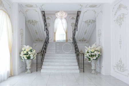 interior elegante real de lujo en estilo barroco. vestíbulo muy luminoso, ligero y blanco con muebles de estilo antiguo caros. elegante amplia escalera de mármol que conduce al segundo piso