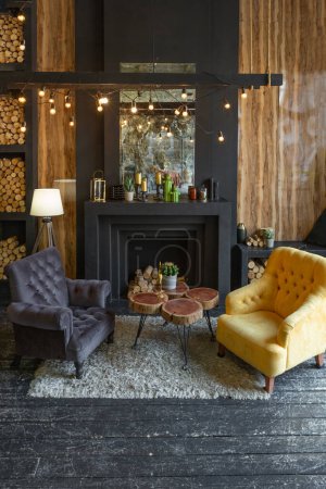 Téléchargez les photos : Intérieur sombre et brutal du salon décoré de bûches de bois. fauteuils doux jaunes et gris, immense fenêtre à arc et cheminée - en image libre de droit