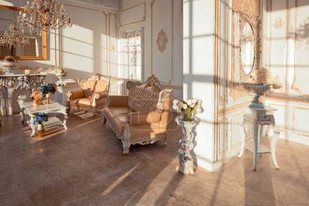 Photo for Rich apartment interior with golden baroque decorations on the walls and luxury furniture. the room is flooded with the rays of the setting sun - Royalty Free Image