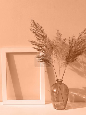 Pfirsichflaum ist die Farbe des Jahres 2024. Rahmen, Glasvase und trockene Blumen in der modischen Mischung rosa-orange Trendfarbe des Jahres Peach Fuzz getönt