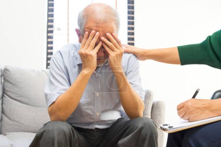 Téléchargez les photos : Déprimé asiatique senior homme partage des problèmes pendant la séance de thérapie avec femme psychiatre écriture sur presse-papiers. - en image libre de droit