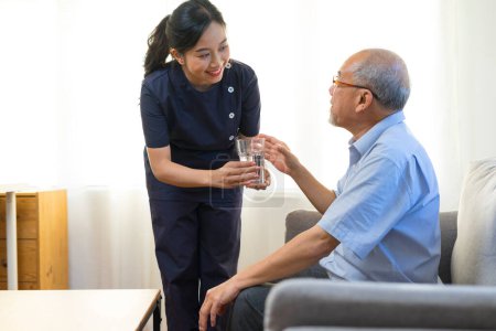 Smiling nurse giving glass of water to senior asian man in nursing home or assisted living facility.