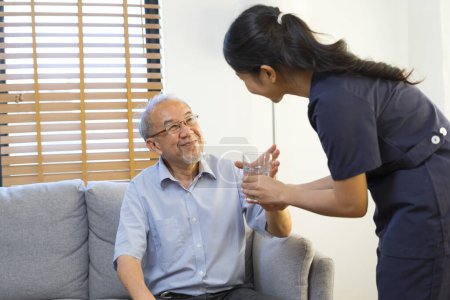 Photo for Smiling nurse giving glass of water to senior asian man in nursing home or assisted living facility. - Royalty Free Image