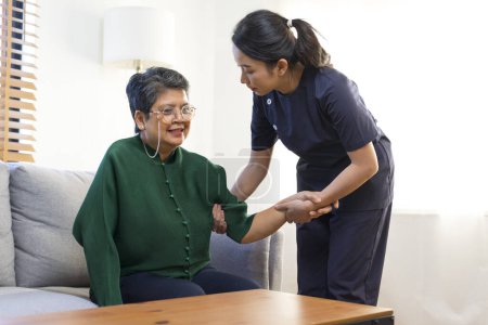 Foto de Mujer asiática enfermera ayudar anciana stand up desde un sofá. - Imagen libre de derechos