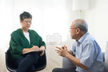 Foto de Deprimido asiático senior hombre compartir problemas durante la sesión de terapia con mujer psiquiatra - Imagen libre de derechos