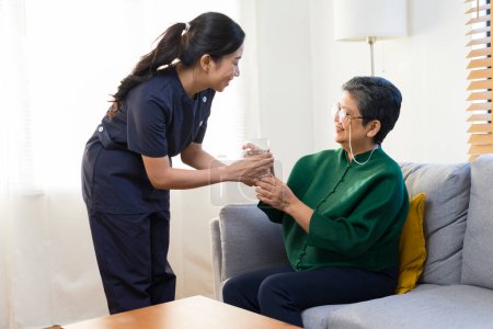 Photo for Smiling nurse giving glass of water to senior asian woman in nursing home or assisted living facility - Royalty Free Image