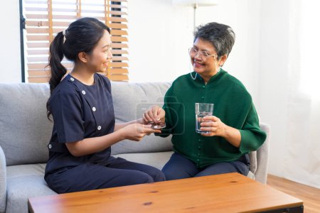 Photo for Smiling nurse giving medicine to senior asian woman in nursing home or assisted living facility - Royalty Free Image