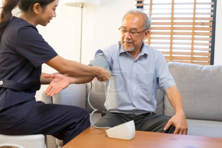 Foto de Joven asiático enfermera hleping senior asiático hombre a comprobar la presión arterial en casa - Imagen libre de derechos