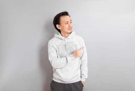 Téléchargez les photos : Casual asiatique homme pointant à droite avec son doigt, gris studio fond - en image libre de droit