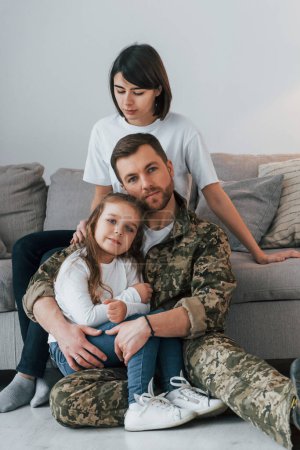 Téléchargez les photos : S'embrasser l'un l'autre. Soldat en uniforme est à la maison avec sa femme et sa fille. - en image libre de droit
