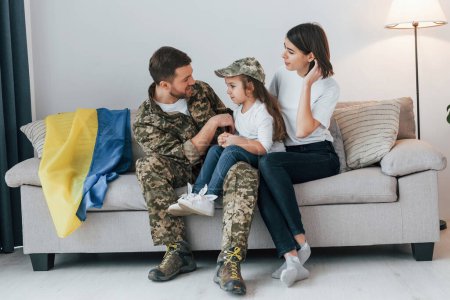 Téléchargez les photos : Supoort Ukraine conception. Soldat en uniforme est à la maison avec sa femme et sa fille. - en image libre de droit