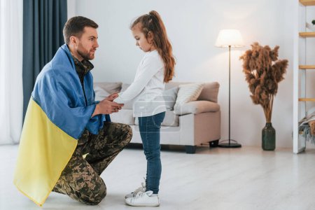 Téléchargez les photos : With Ukrainian flag. Soldier in uniform is at home with his little daughter. - en image libre de droit