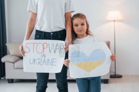 Téléchargez les photos : Mère avec sa petite fille debout avec des bannières avec texte arrêter la guerre à Ukrane. - en image libre de droit