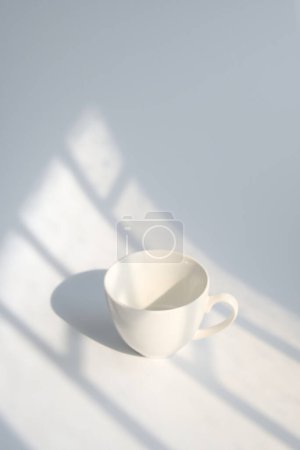 Light and shadow fall from the window onto a white cup.