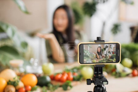 Photo for Exotic tropical healthy food concept. Beautiful smiling asian young woman blogger in traditional conical hat cooking fresh organic healthy food using hazelnuts indoor at exotic tropical home studio. - Royalty Free Image