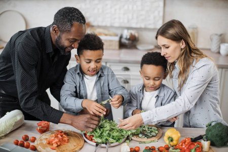 Großaufnahme von Eltern und ihren Söhnen, die in der Küche gemeinsam Essenssalat zubereiten. Glückliche Jungen Kinder helfen Mama und Papa, helfen beim Abendessen oder Mittagessen und reißen Salatblätter in Schale.