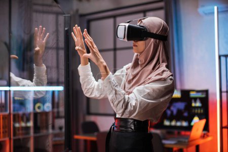 Foto de Confident muslim woman in hijab using innovative technology during business strategy. Young female company workers wearing VR headset while having meeting at office room. - Imagen libre de derechos