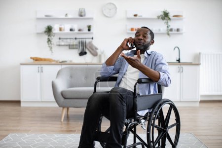 Photo for Close up view of african male with mobility impairment being involved in phone talk while relaxing in home interior. Confident person discussing after dinner activity with friends outside apartment. - Royalty Free Image