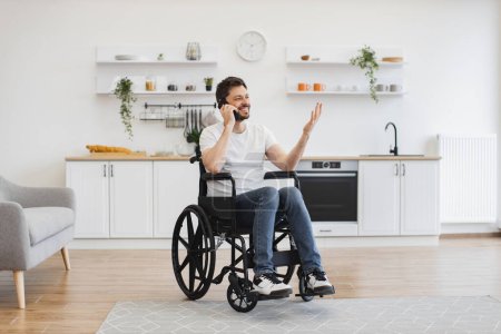 Photo for Full length view of adult person in wheelchair talking on cell phone while using comfort of modern studio flat. Mature Caucasian man organising birthday party while getting recovery from illness. - Royalty Free Image