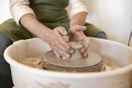 Erwachsene männliche Töpfer beschäftigen sich mit der Kunst, eine Keramikschale mit einer Töpferscheibe zu modellieren und dabei Geschick und Präzision unter Beweis zu stellen.