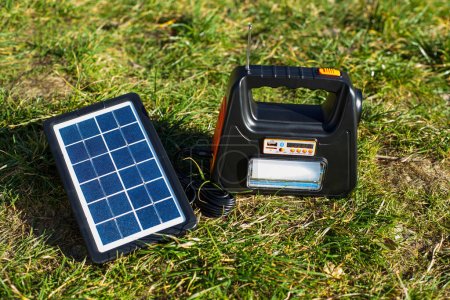 Téléchargez les photos : Une borne de recharge portable avec une lampe de poche est chargée à partir d'un panneau solaire dans la nature. La batterie pour charger les gadgets est chargée par temps ensoleillé. - en image libre de droit