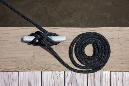 Photo for A black mooring rope with a knotted end tied around a cleat on a wooden pier. - Royalty Free Image