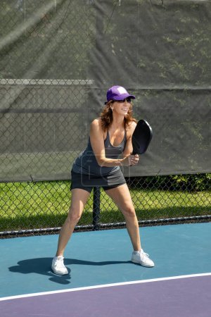 A pickleball player prepares for a return of serve on a suburban pickleball court during summer.