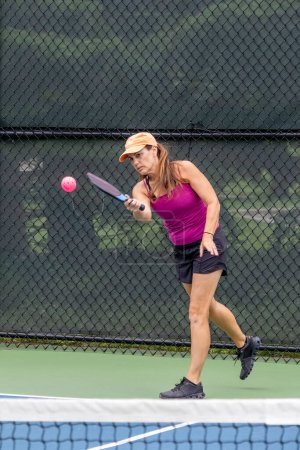 A pickleball player serves the ball on a suburban pickleball court during summer.