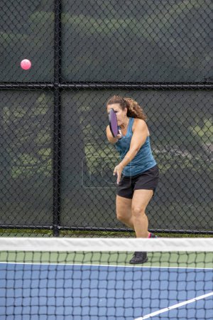 A pickleball player serves the ball on a suburban pickleball court during summer.