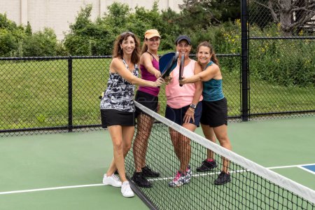 Four female pickleball players touch paddles after a competitive game.