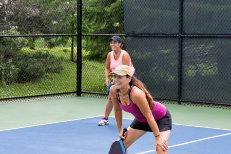 Two smiling pickleball players prepare for action on a suburban pickleball court during summer.