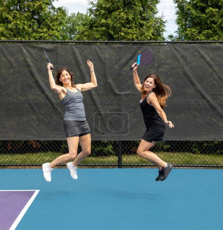 Two pickleball players jumping with paddles on a court during summer.