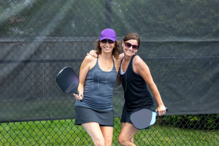 Two pickleball players posing with paddles on a court during summer.
