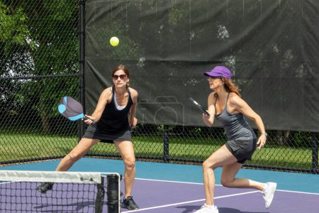 Two pickleball players prepare to return a ball on a suburban pickleball court during summer.