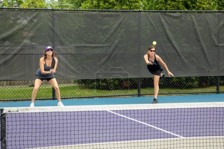 A pickleball player serves the ball as her partner gets ready for a return.
