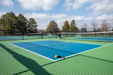 View of a pickleball complex with a paddle and yellow on blue and green courts beside a playground in a suburban park in early spring.