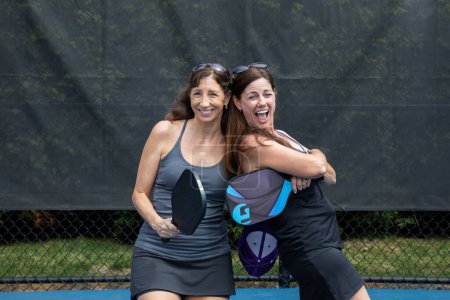 Two pickleball players posing with paddles on a court during summer.