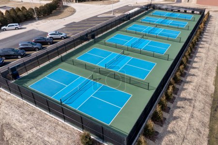 Aerial view of a new pickleball facility with blue and green courts in a suburban park in early spring.