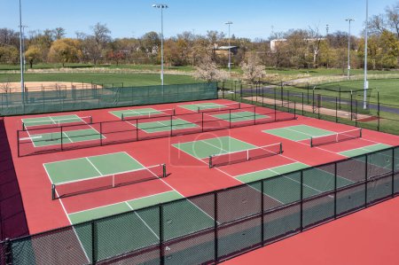 Aerial view of a pickleball facility with red and green courts in a suburban park in spring.