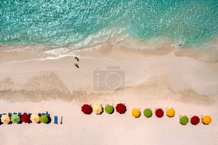 Foto de Vista aérea de coloridas sombrillas a lo largo de una playa con dos caminantes en la bahía de Rendezvous en Anguila. - Imagen libre de derechos