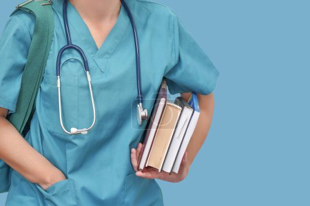 Nahaufnahme einer jungen Doktorandin mit Stethoskop und Büchern in der Hand auf blauem Hintergrund. Krankenschwester, Studentin, Ausbildung. Medizinstudentin an der Universität. Medizinische Ausbildung