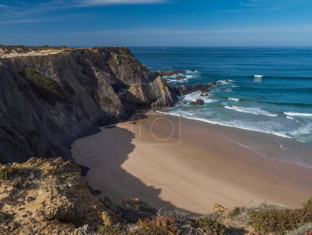 Photo for View of empty Praia da Amalia beach with ocean waves, cliffs and stones, wet golden sand and green vegetation at wild Rota Vicentina coast, Odemira, Portugal - Royalty Free Image