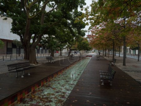 Foto de Lisboa, Portugal, 30 de octubre de 2021: callejón de árboles y fuente de agua Vulcao de agua en Alameda dos Oceanos en Moscavide, Lisboa, día lluvioso de otoño. - Imagen libre de derechos
